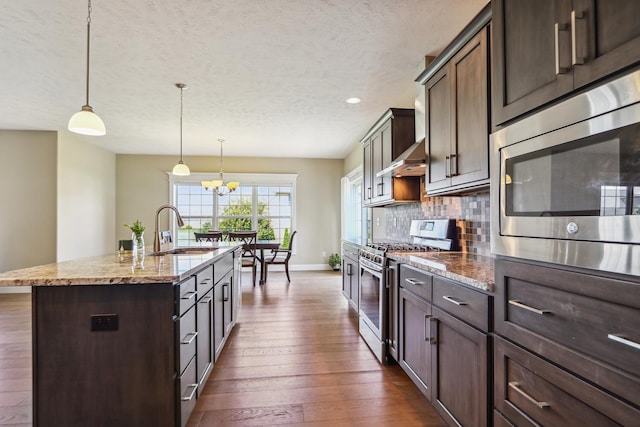 kitchen featuring a center island with sink, decorative backsplash, dark wood-style floors, stainless steel appliances, and a sink