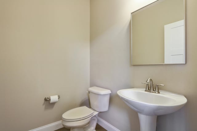 half bath featuring toilet, baseboards, and a sink