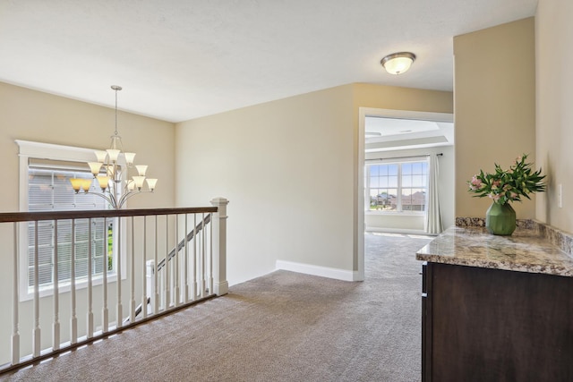 hall featuring baseboards, an upstairs landing, carpet, and an inviting chandelier