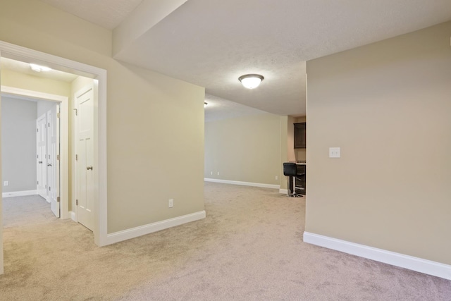 empty room with light carpet, a textured ceiling, and baseboards