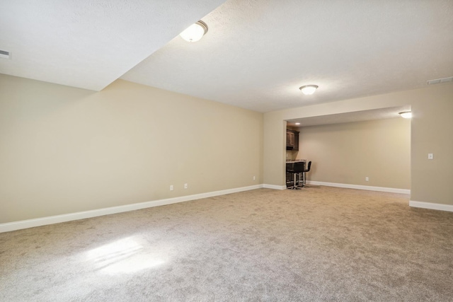 basement with a bar, visible vents, light colored carpet, and baseboards