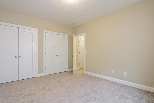 unfurnished bedroom featuring baseboards, multiple closets, carpet, and a textured ceiling