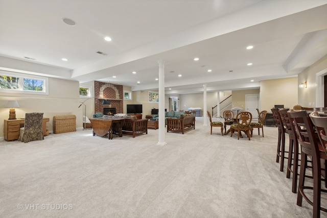 carpeted living room with a brick fireplace and ornate columns