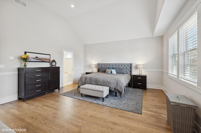 bedroom with light hardwood / wood-style floors, lofted ceiling, and ensuite bath