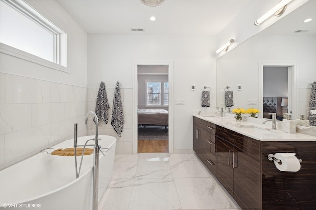 bathroom with vanity, a bath, and tile walls