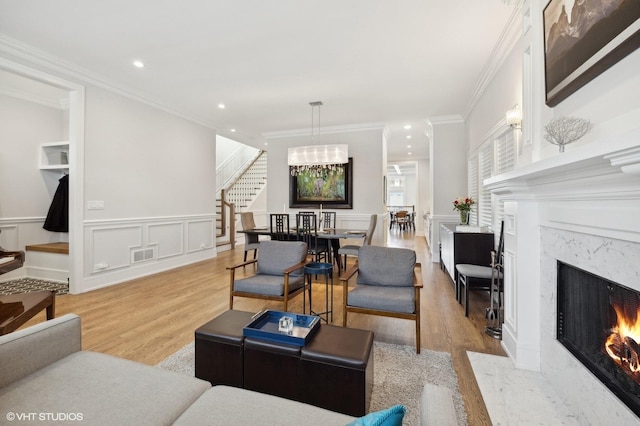 living room featuring a high end fireplace, light hardwood / wood-style floors, and ornamental molding