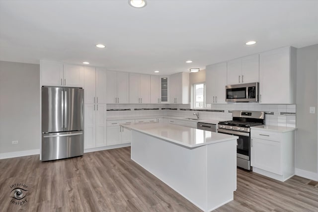 kitchen with light wood-type flooring, appliances with stainless steel finishes, white cabinets, sink, and tasteful backsplash