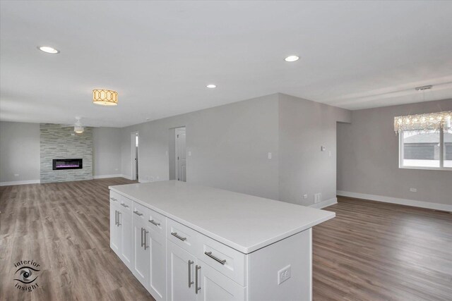 kitchen featuring hanging light fixtures, a kitchen island, hardwood / wood-style flooring, white cabinets, and a large fireplace