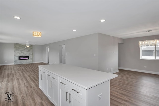 kitchen with a center island, white cabinetry, hanging light fixtures, wood-type flooring, and a large fireplace