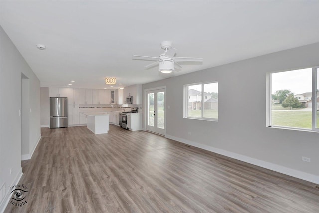 unfurnished living room featuring light wood-type flooring, baseboards, and a ceiling fan