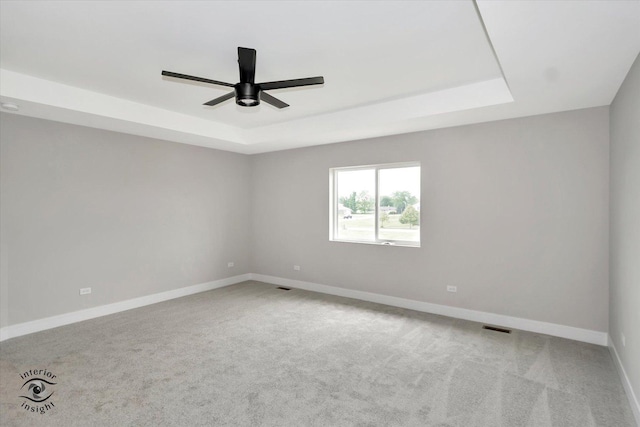 spare room with a tray ceiling, carpet, visible vents, and baseboards