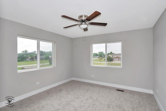 carpeted spare room featuring a ceiling fan, visible vents, and baseboards