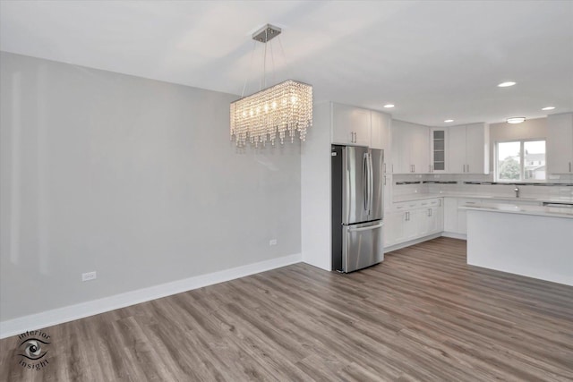 kitchen with wood finished floors, baseboards, light countertops, freestanding refrigerator, and glass insert cabinets