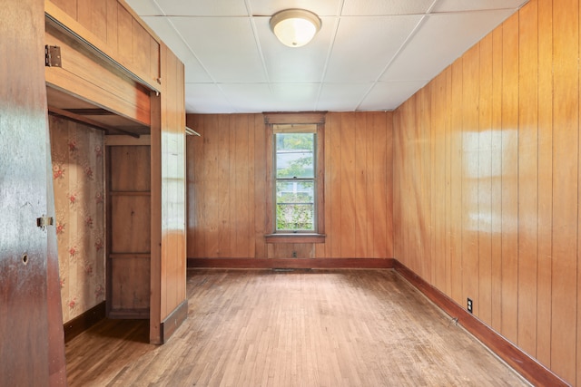 unfurnished room with wood walls, hardwood / wood-style flooring, and a paneled ceiling