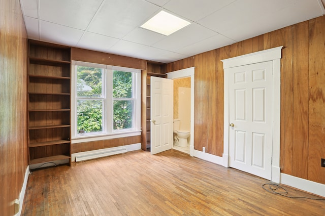 unfurnished bedroom with a baseboard heating unit, wood walls, light hardwood / wood-style flooring, and multiple windows