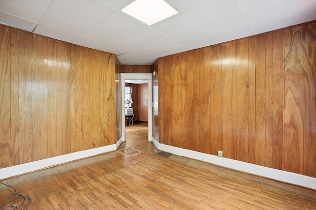 empty room featuring a paneled ceiling, hardwood / wood-style flooring, and wooden walls