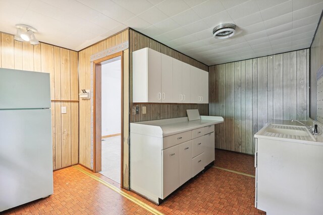 kitchen with wood walls, sink, white cabinetry, and white refrigerator