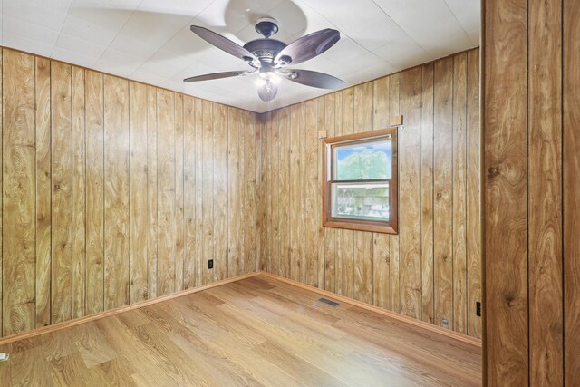 empty room with light hardwood / wood-style floors, ceiling fan, and wood walls