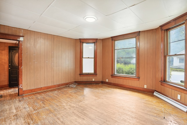 unfurnished room with wood walls, a baseboard radiator, wood-type flooring, and a paneled ceiling