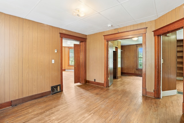 unfurnished room featuring wooden walls, a drop ceiling, and hardwood / wood-style floors