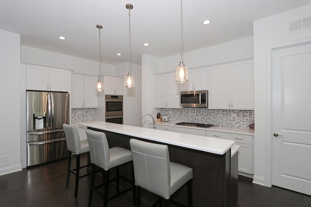 kitchen featuring a kitchen breakfast bar, hanging light fixtures, an island with sink, appliances with stainless steel finishes, and white cabinetry