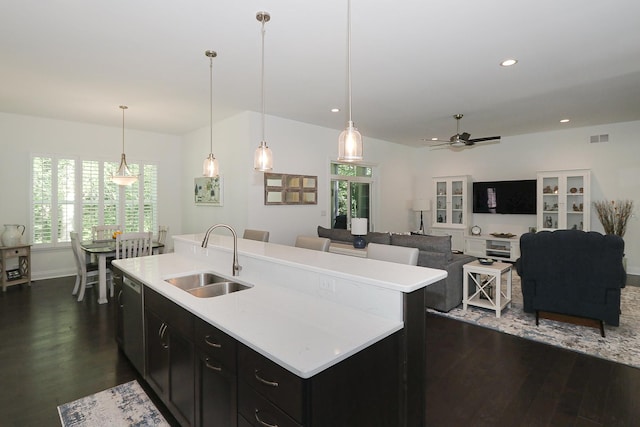 kitchen with ceiling fan, sink, hanging light fixtures, dark hardwood / wood-style floors, and a center island with sink