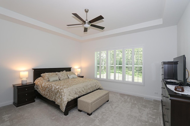 bedroom featuring light carpet, a raised ceiling, and ceiling fan