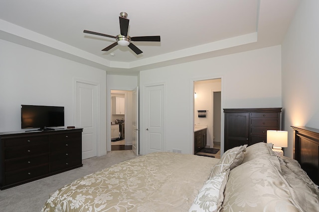 bedroom with a raised ceiling, connected bathroom, ceiling fan, and light colored carpet