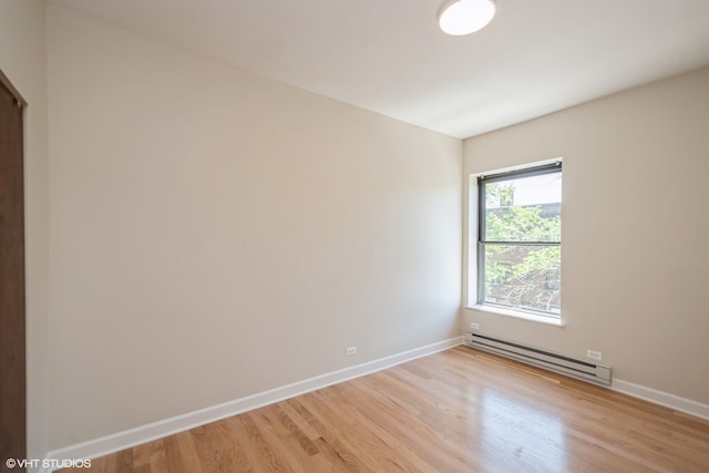 spare room featuring baseboard heating and light hardwood / wood-style floors