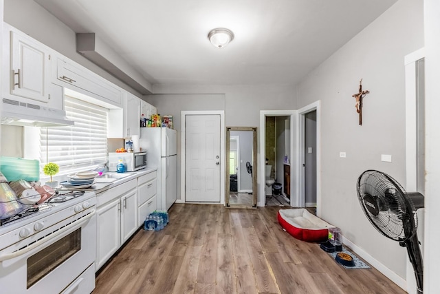 kitchen with light countertops, white cabinets, under cabinet range hood, and white gas range