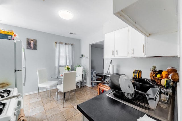 kitchen with white cabinets, dark countertops, stove, freestanding refrigerator, and light tile patterned flooring