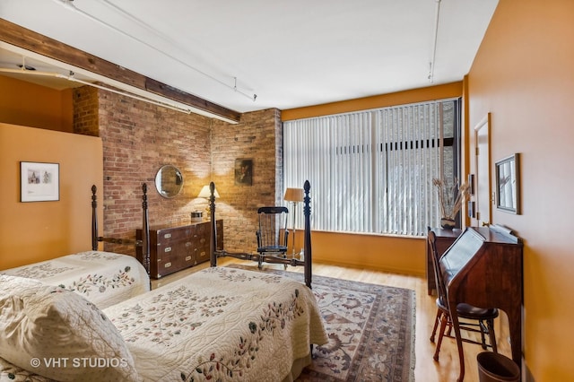 bedroom featuring beamed ceiling, brick wall, and light hardwood / wood-style flooring