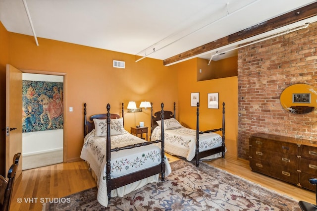 bedroom featuring brick wall and light hardwood / wood-style flooring