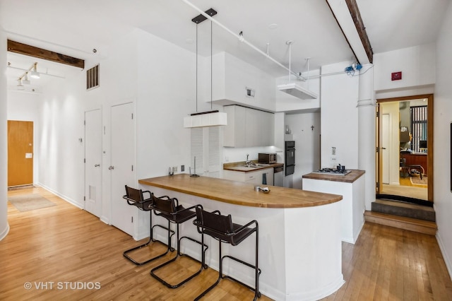 kitchen featuring light hardwood / wood-style flooring, white cabinetry, hanging light fixtures, kitchen peninsula, and beamed ceiling