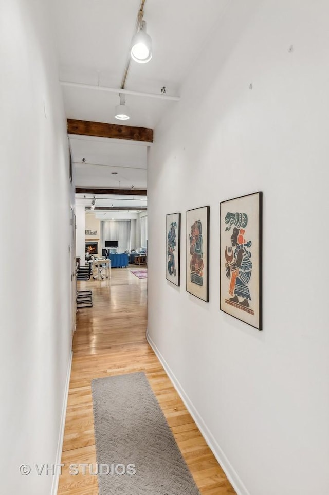 hallway featuring beamed ceiling, wood-type flooring, and rail lighting