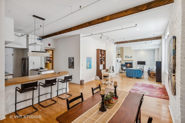 dining space featuring track lighting, beam ceiling, and light hardwood / wood-style floors