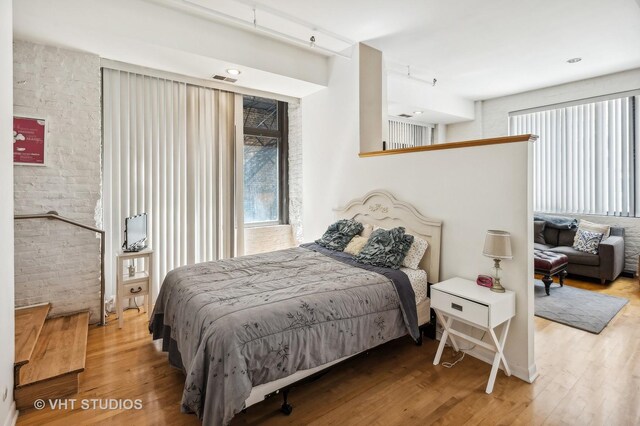 bedroom with wood-type flooring and brick wall