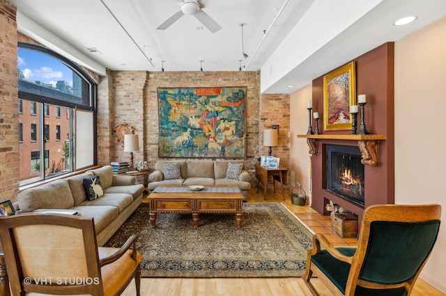 living room featuring ceiling fan, brick wall, rail lighting, and light hardwood / wood-style flooring