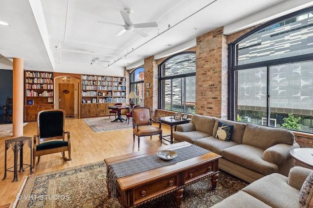 living room with brick wall, built in features, rail lighting, hardwood / wood-style flooring, and ceiling fan