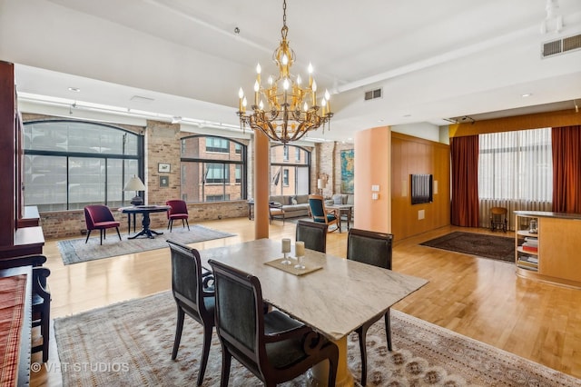 dining room with a notable chandelier, brick wall, and light wood-type flooring