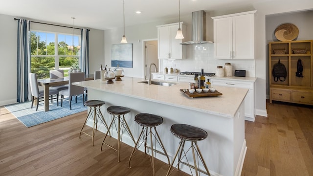 kitchen featuring wall chimney range hood, hanging light fixtures, sink, and light hardwood / wood-style flooring