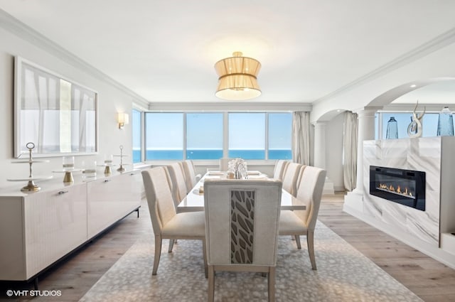 dining area featuring a water view, a fireplace, crown molding, and light wood-type flooring