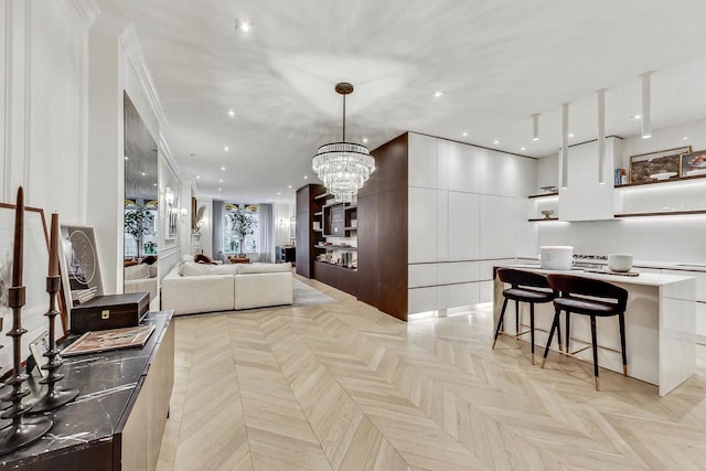 interior space featuring a breakfast bar, crown molding, an inviting chandelier, white cabinetry, and light parquet flooring