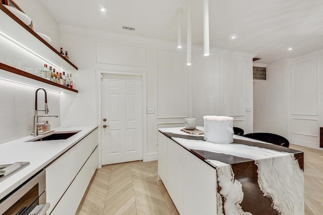 kitchen with white cabinetry, light parquet floors, ornamental molding, and sink