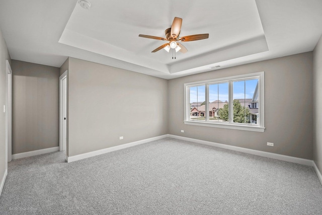 carpeted spare room featuring a tray ceiling and ceiling fan