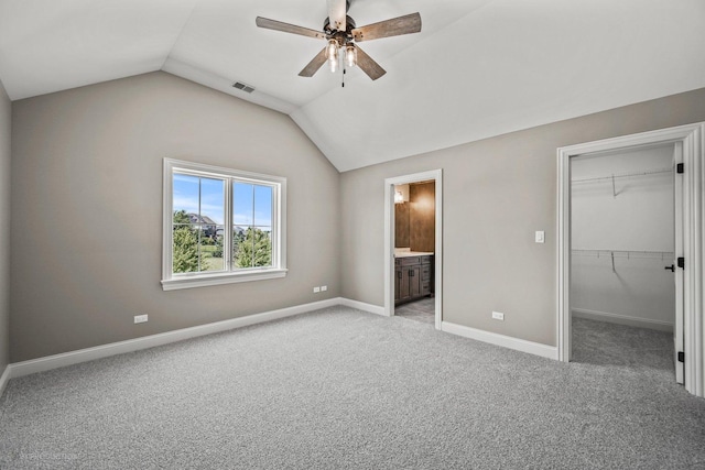 unfurnished bedroom with lofted ceiling, ensuite bathroom, a walk in closet, ceiling fan, and a closet