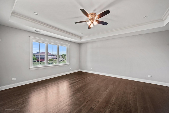 empty room featuring dark hardwood / wood-style flooring, a tray ceiling, ceiling fan, and ornamental molding