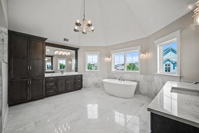 bathroom with an inviting chandelier, high vaulted ceiling, a bathtub, vanity, and tile walls