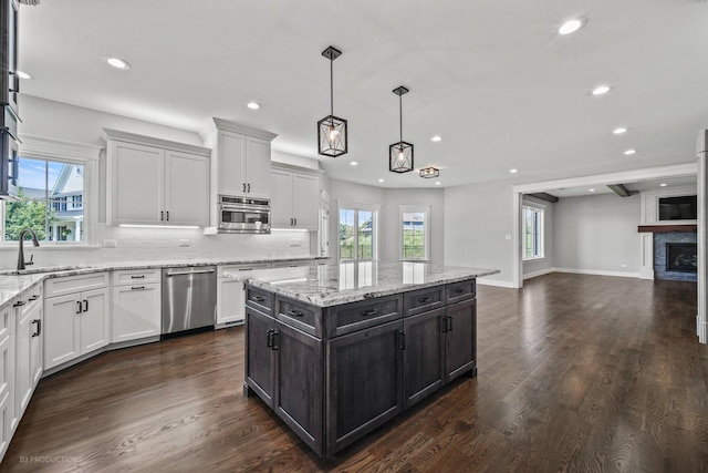 kitchen with a stone fireplace, white cabinetry, sink, and appliances with stainless steel finishes