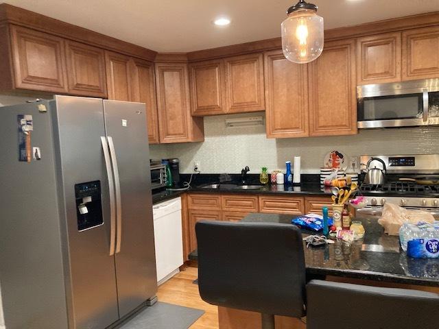 kitchen with pendant lighting, sink, decorative backsplash, light wood-type flooring, and appliances with stainless steel finishes